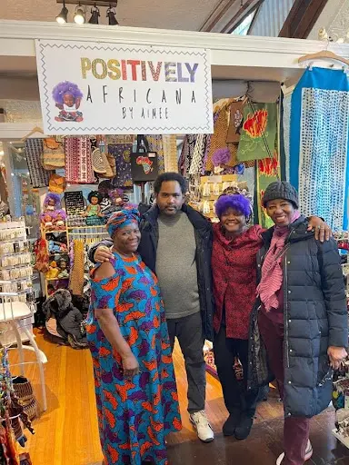 Store community moment — Aimee with visitors, full product display, vibrant signage, authentic energy